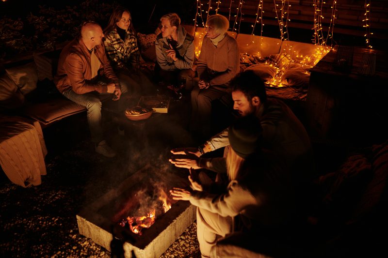 People eating outdoors around a fire in the evening