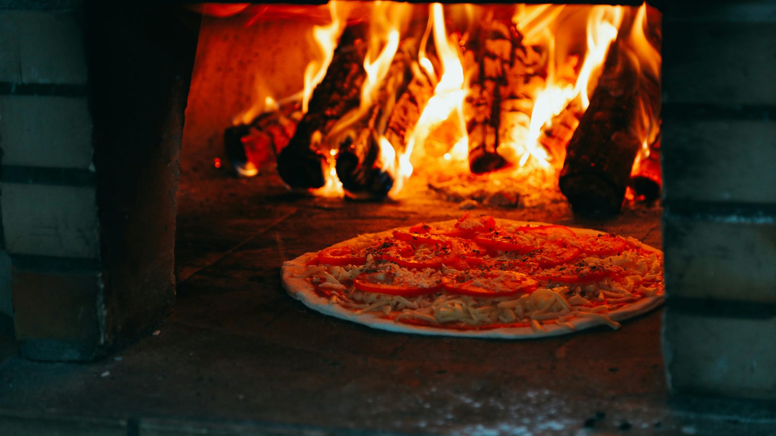 A pizza cooking in a wood-fired outdoor oven
