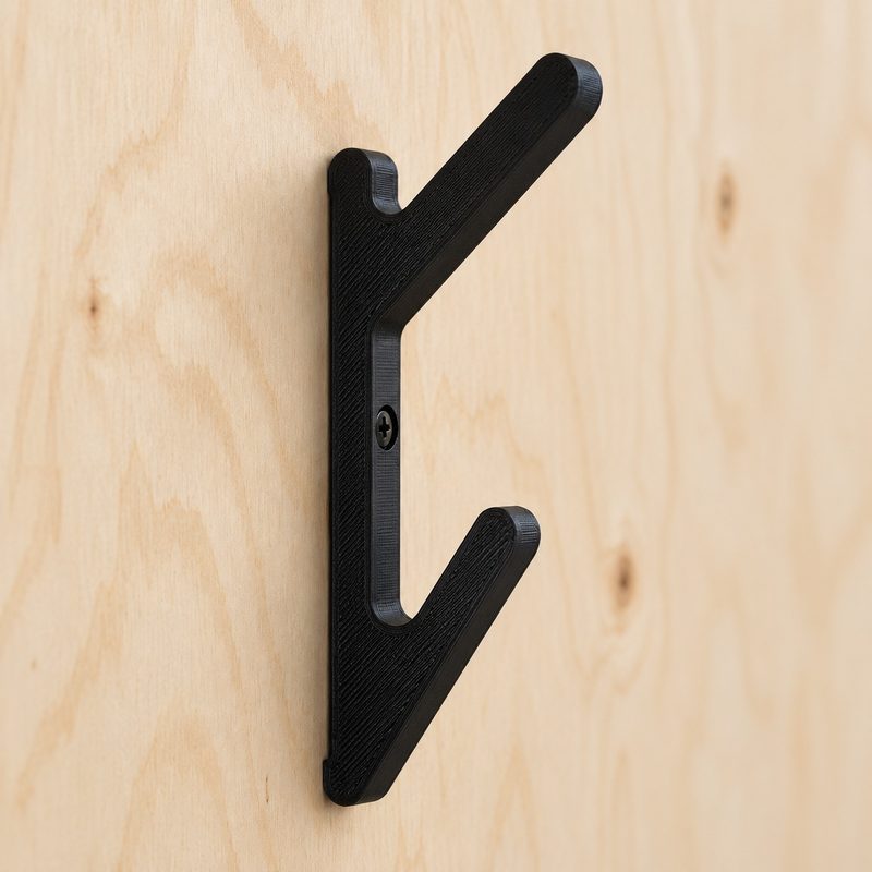 A black angled double hook screwed to a plywood wall